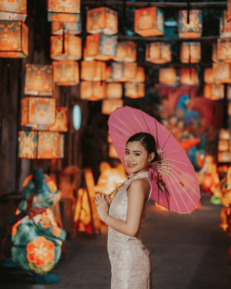 Traveller holding a pink umbrella beneath glowing lanterns in Malaysia